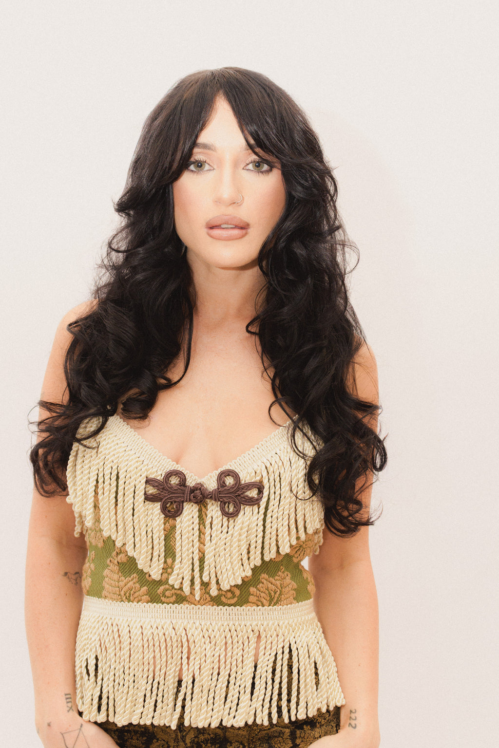 Woman wearing a fringed top with a decorative frog closure on a plain background