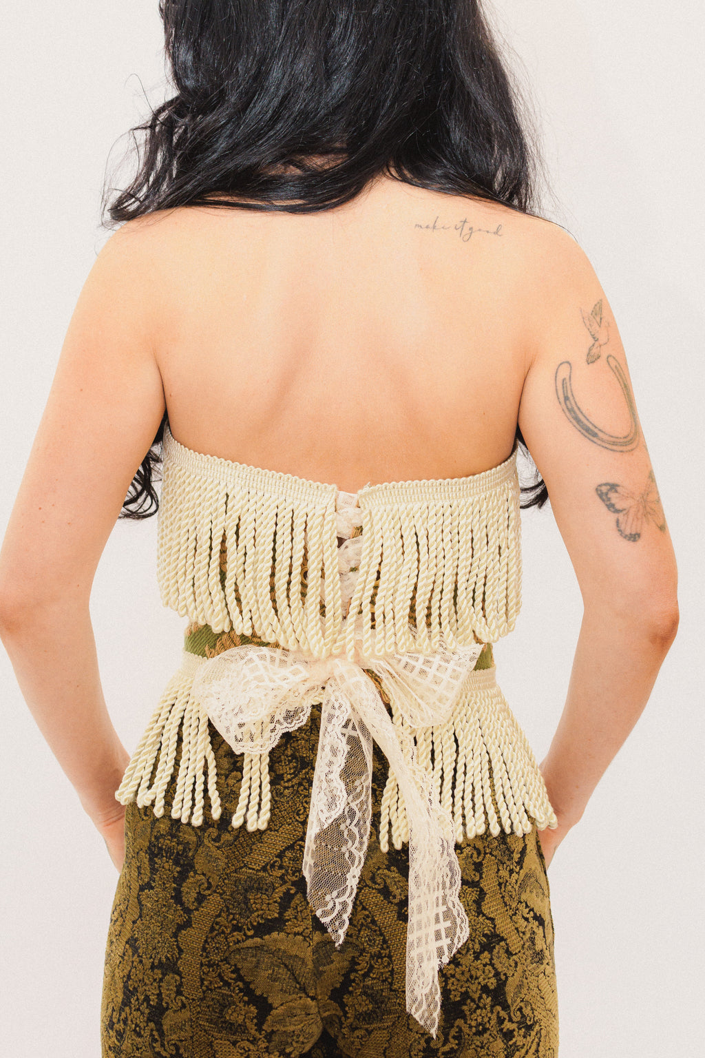 Person wearing a beige fringed top with lace details on a plain background