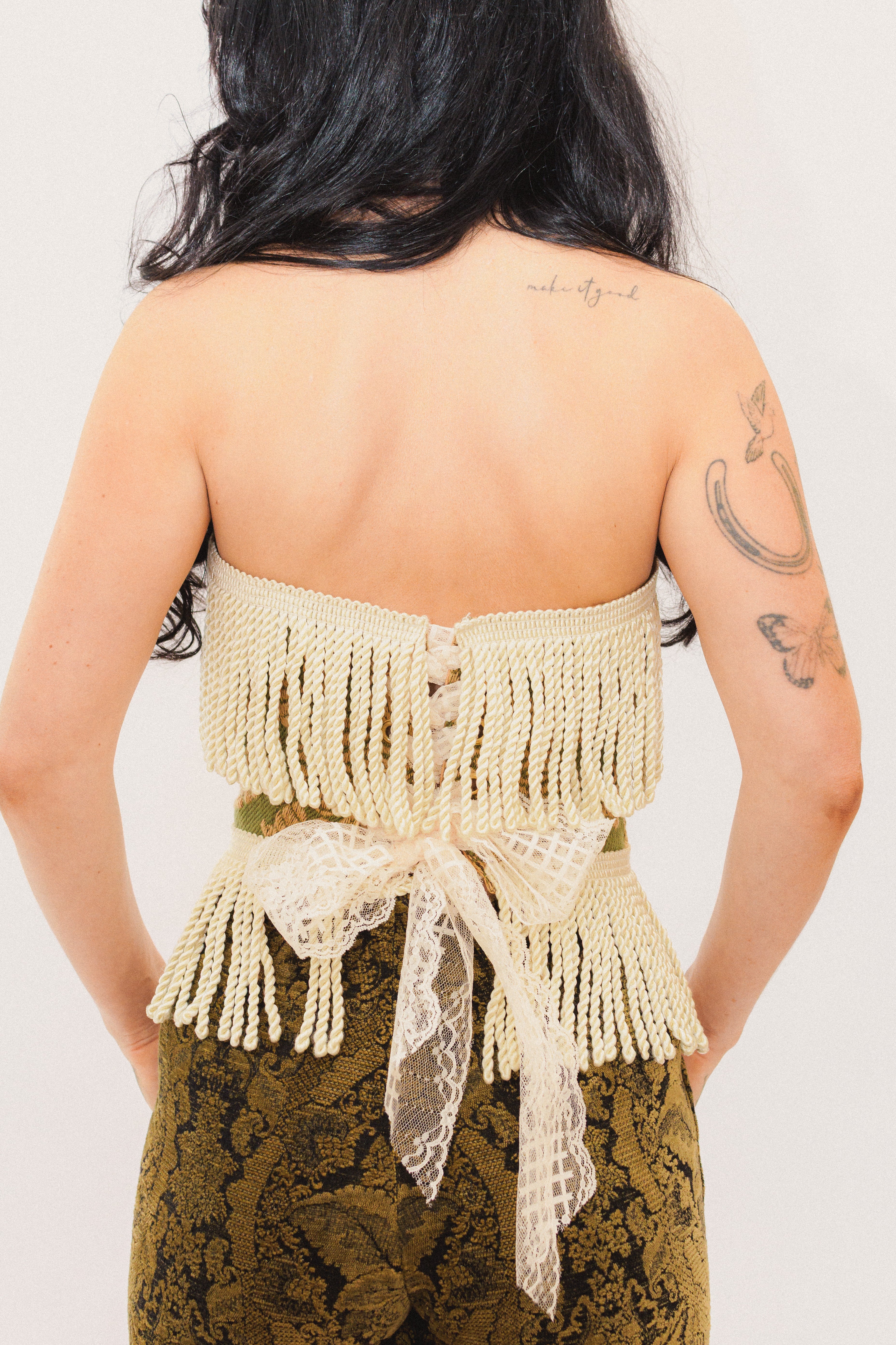 Person wearing a beige fringed top with lace details on a plain background