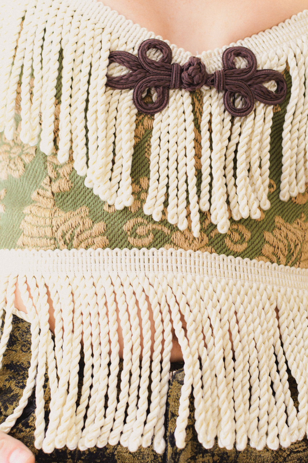Close-up of a brocade corset top with fringe trim and a brown frog closure