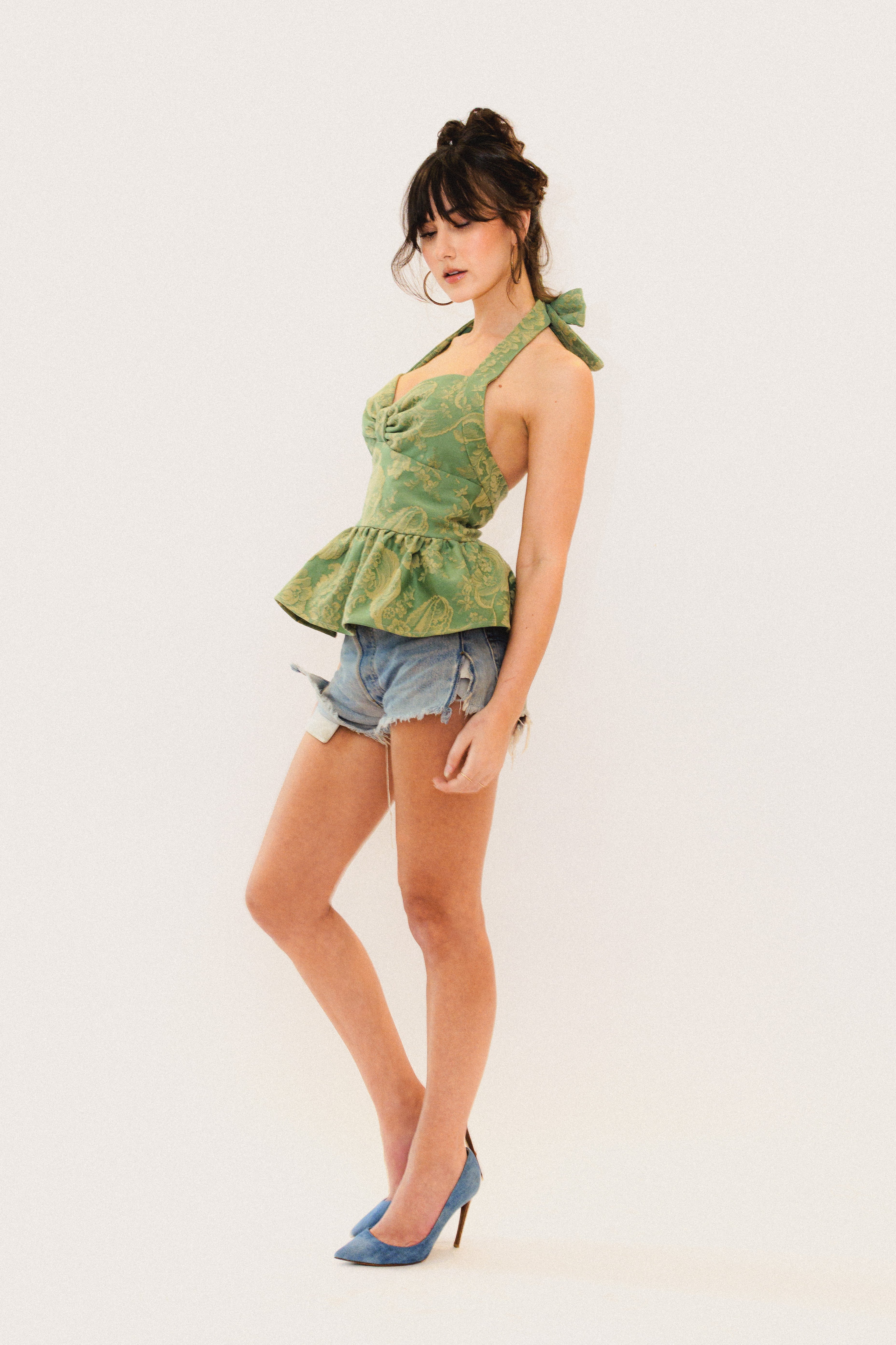 Woman wearing a green patterned top and denim shorts on a white background
