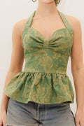 Woman wearing a green patterned halter top and denim shorts on a white background