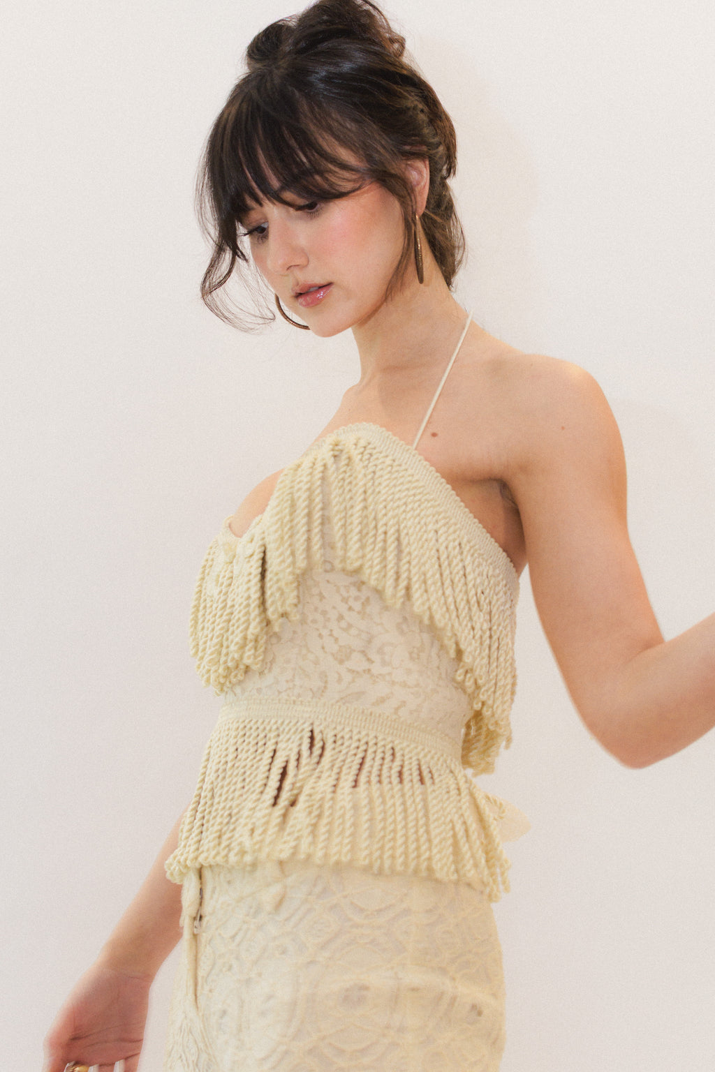 Woman wearing a cream fringe corset top against a plain background