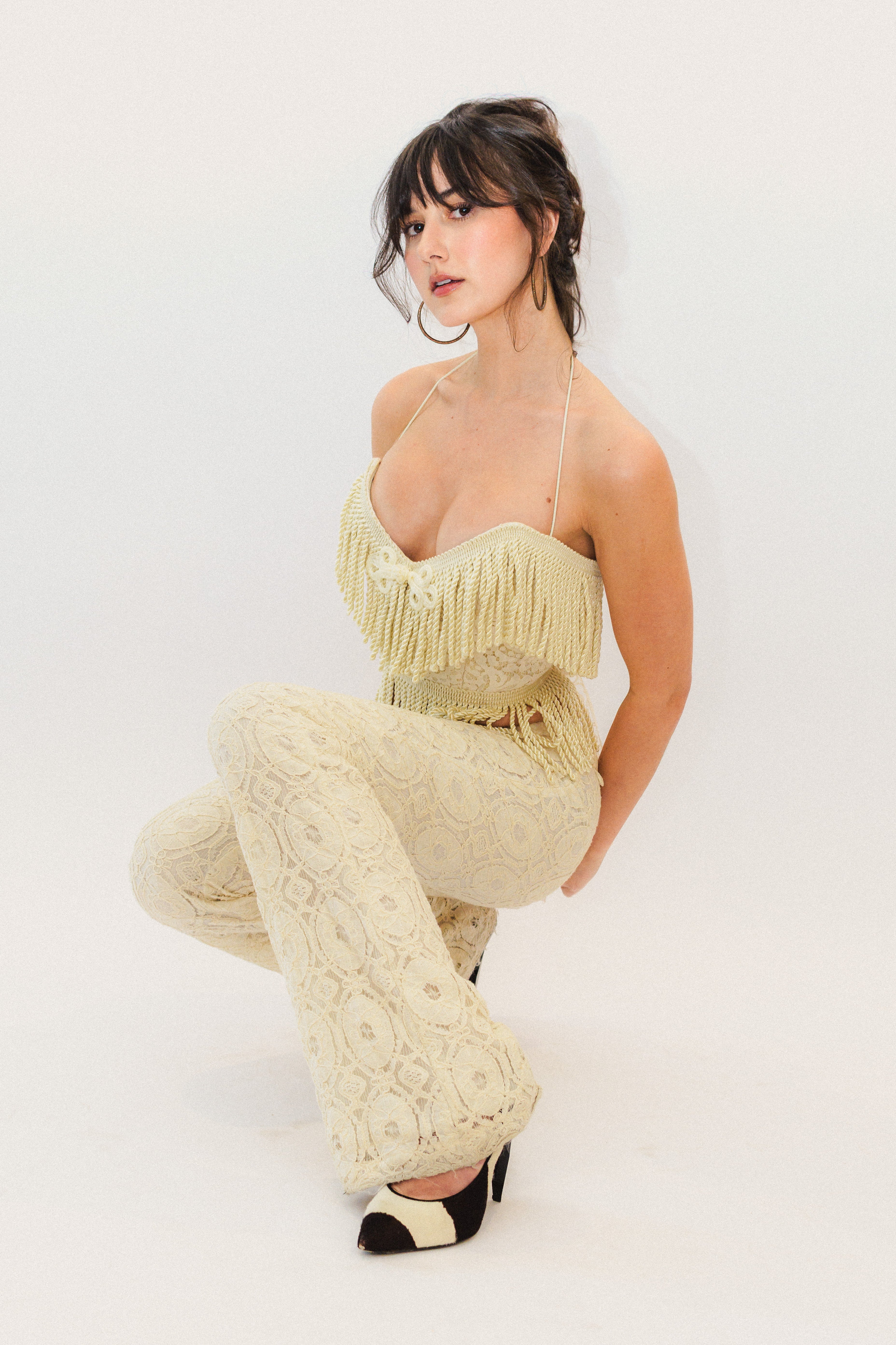 Woman wearing a cream fringe corset top and pants on a white background