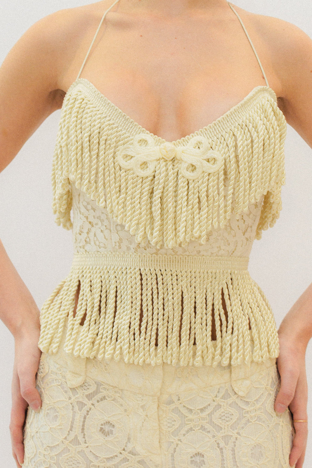 Woman wearing a cream lace fringe corset top against a white background