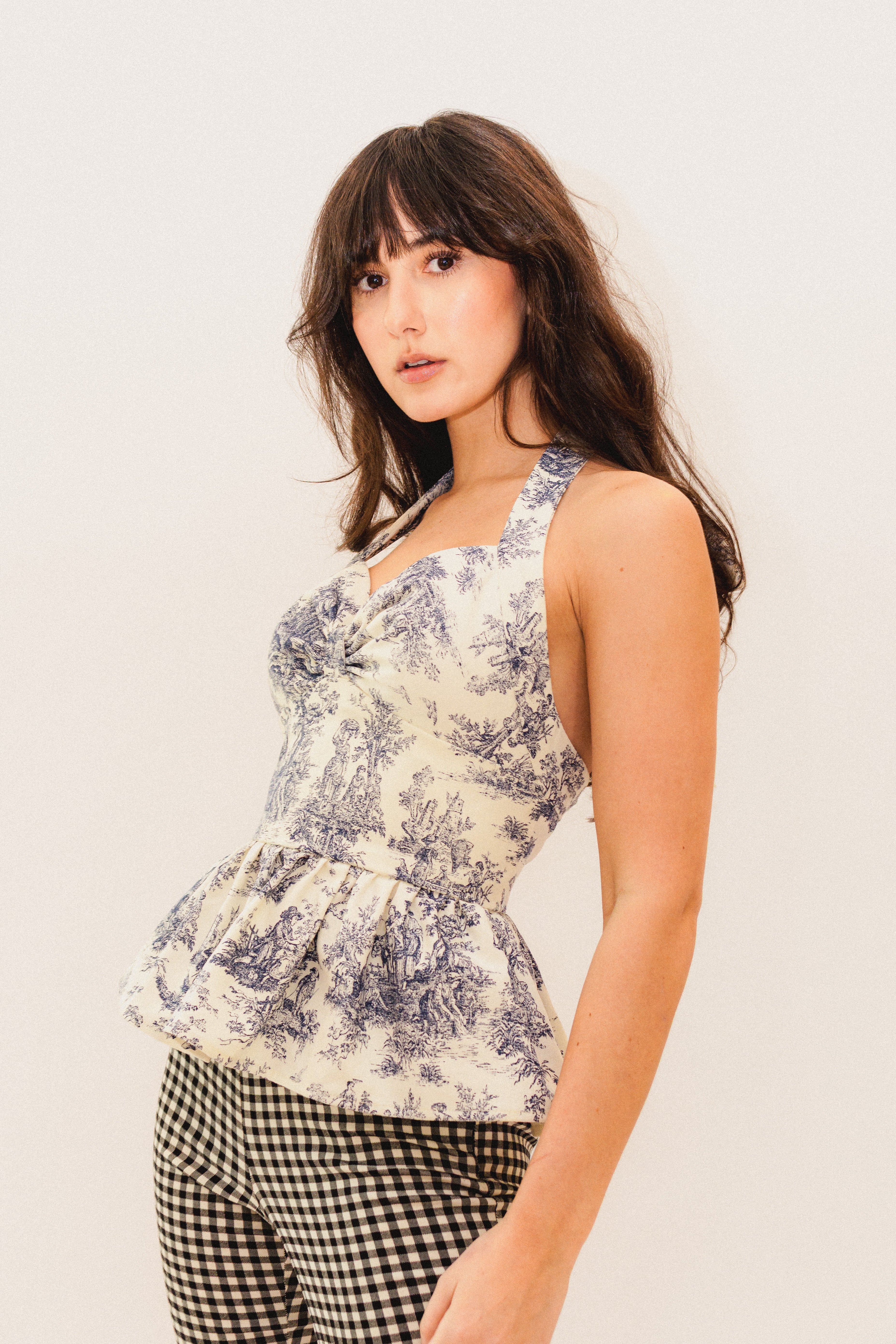 Woman wearing a black and white toile de jouy peplum halter top and checkered pants against a plain background