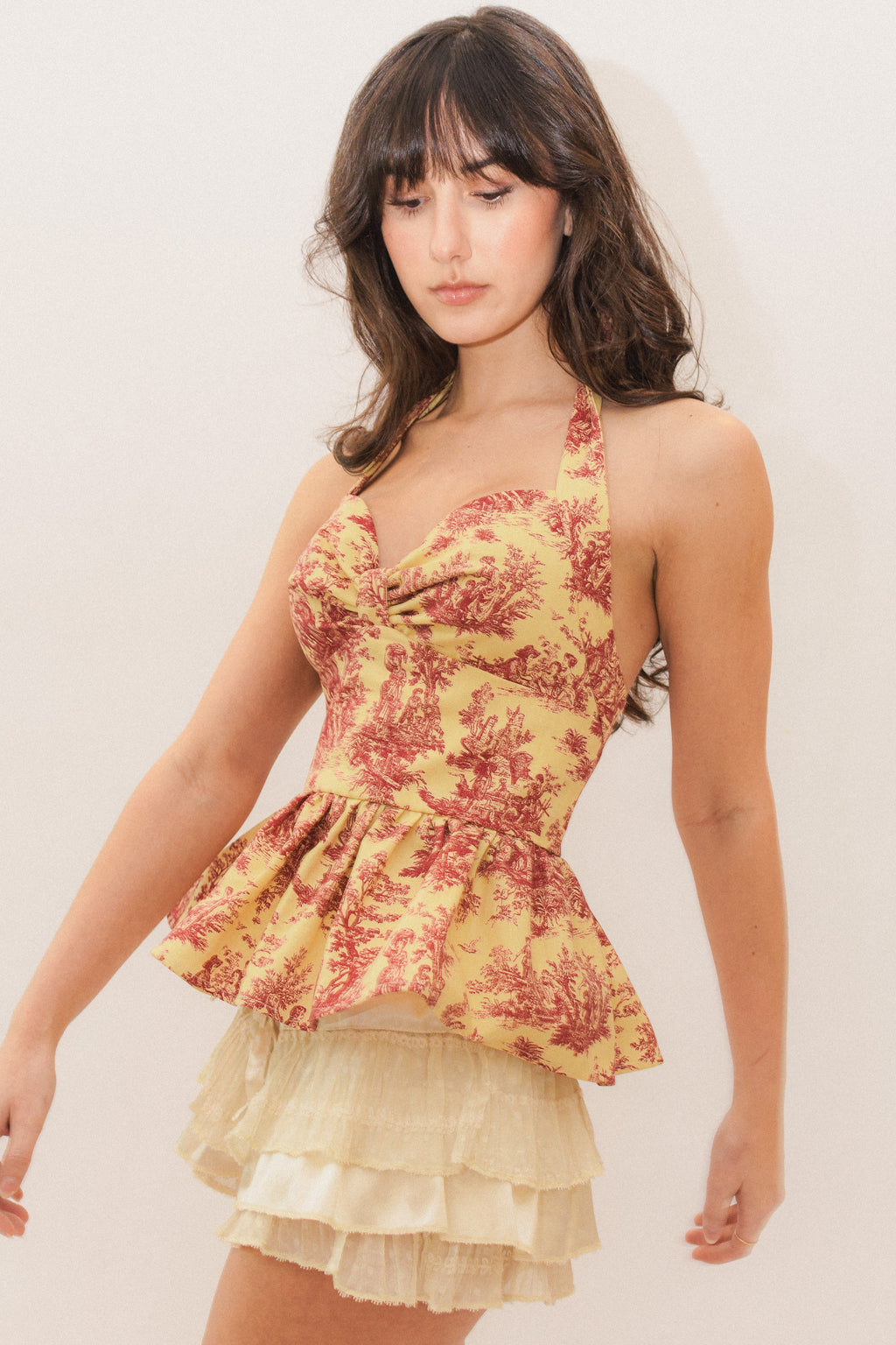 Woman wearing a yellow and red toile de jouy halter peplum top with white ruffled bloomer shorts on a plain background