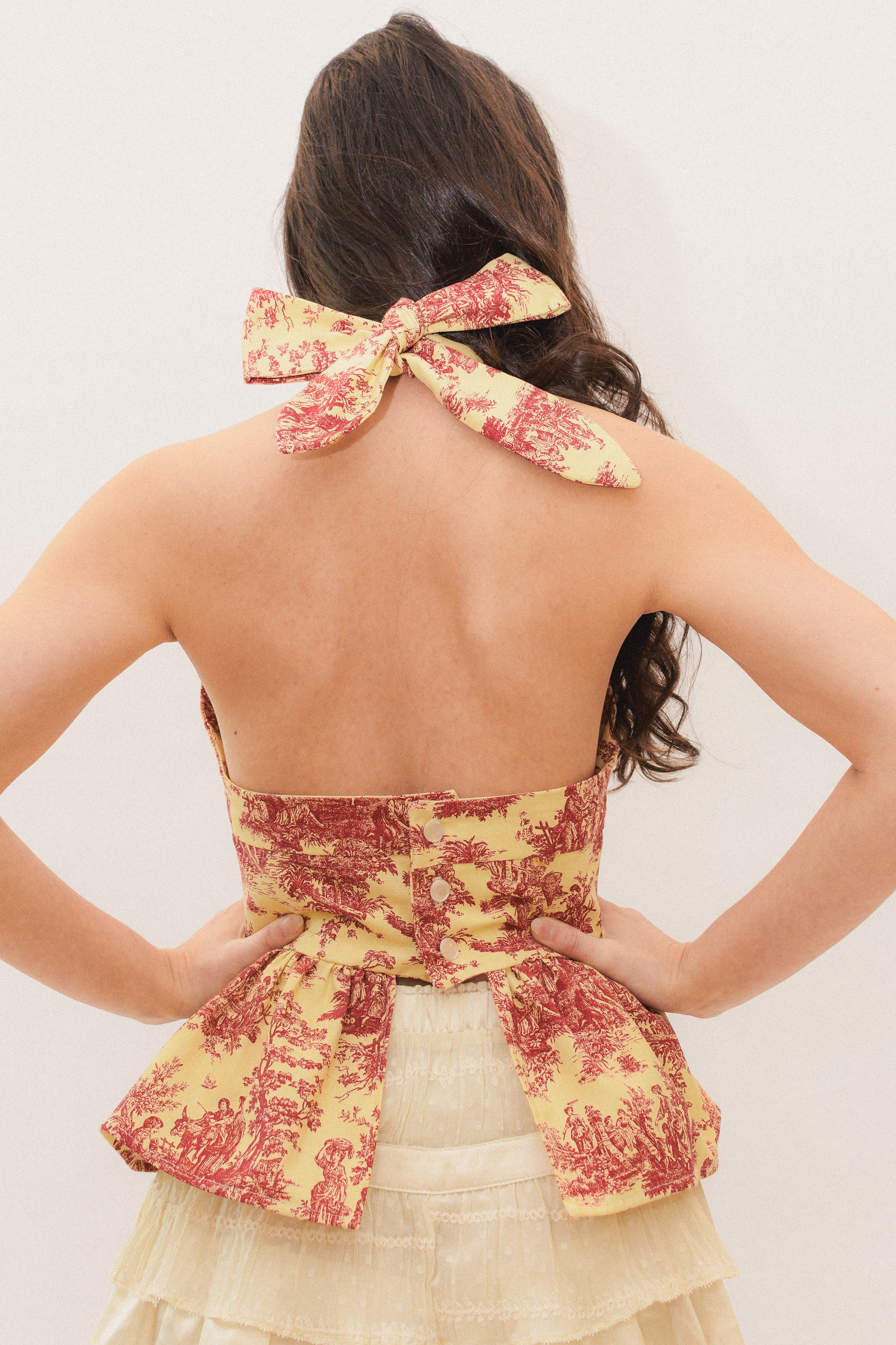 Woman wearing a yellow and red patterned halter top with a bow detail on a plain background