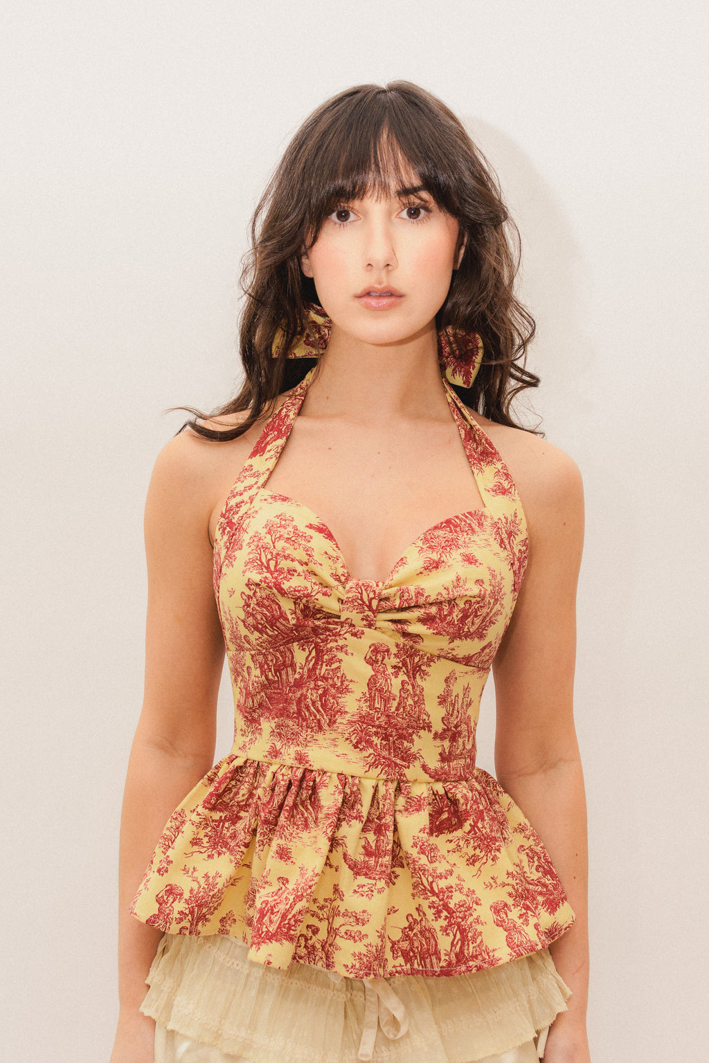 Woman wearing a yellow and red toile de jouy halter peplum top against a plain background