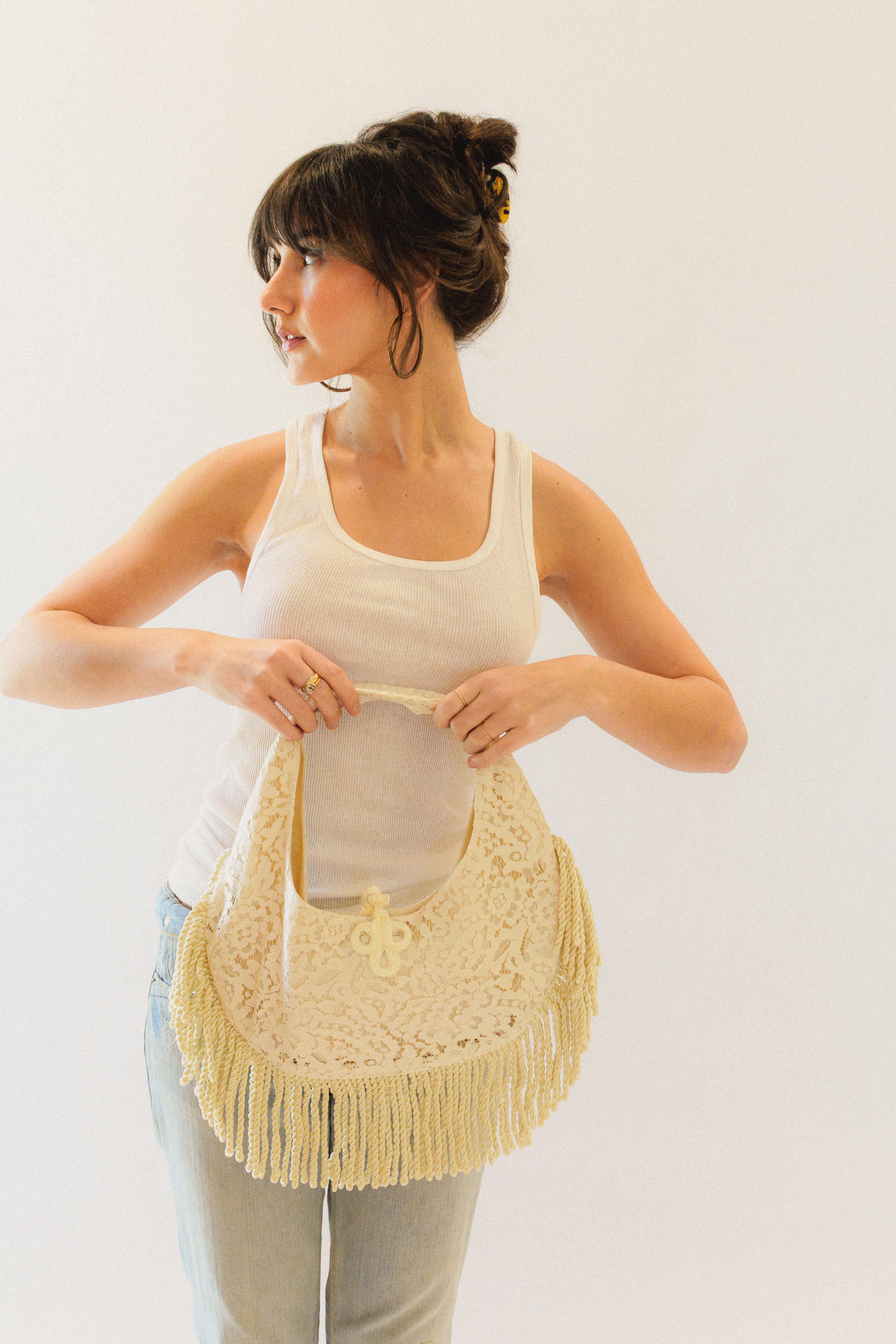 Woman holding a cream lace handbag with fringe details against a white background