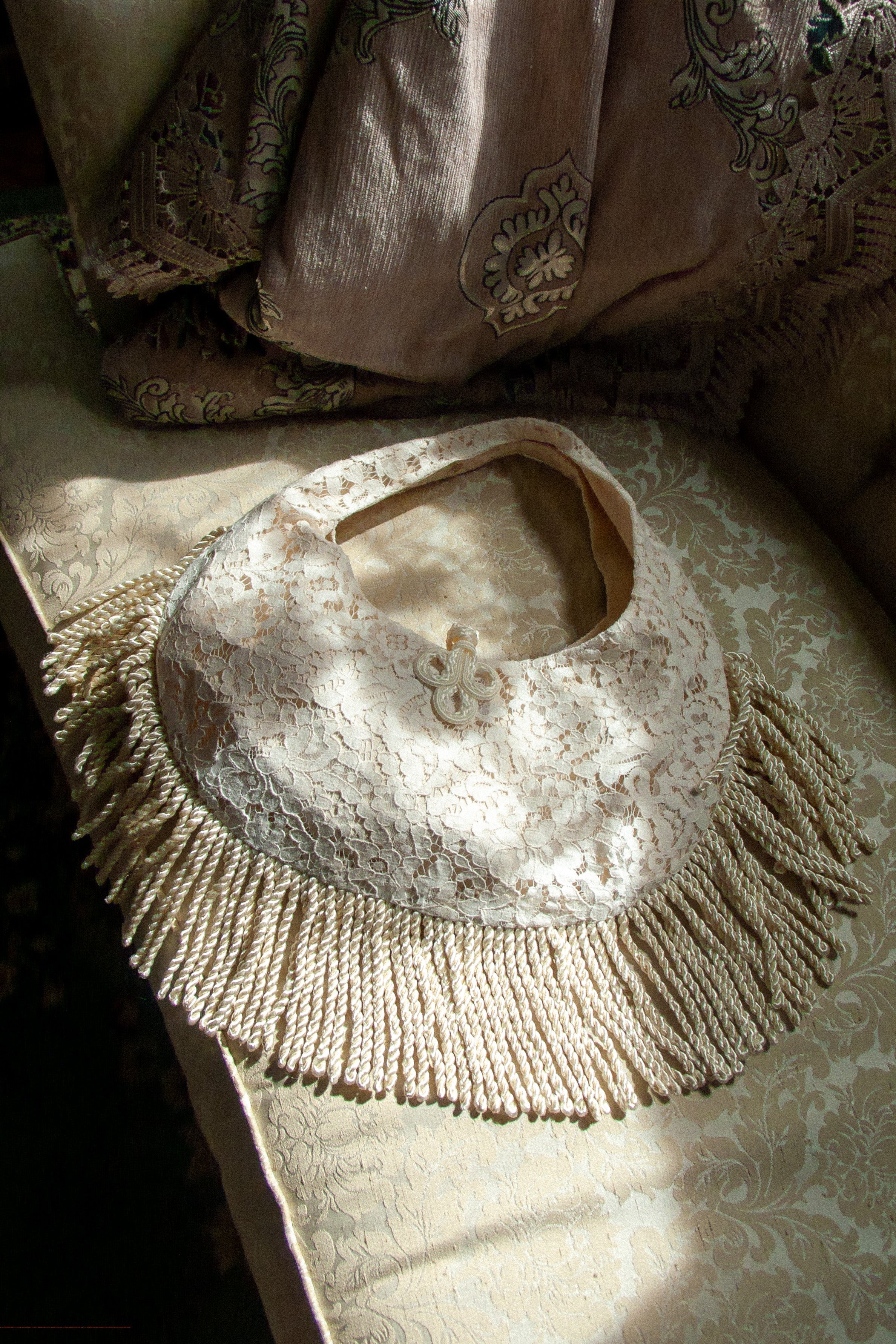 cream lace handbag with frog closure and fringe on a vintage brocade couch