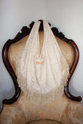 Cream lace tote bag with fringe on an ornate chair against a plain wall