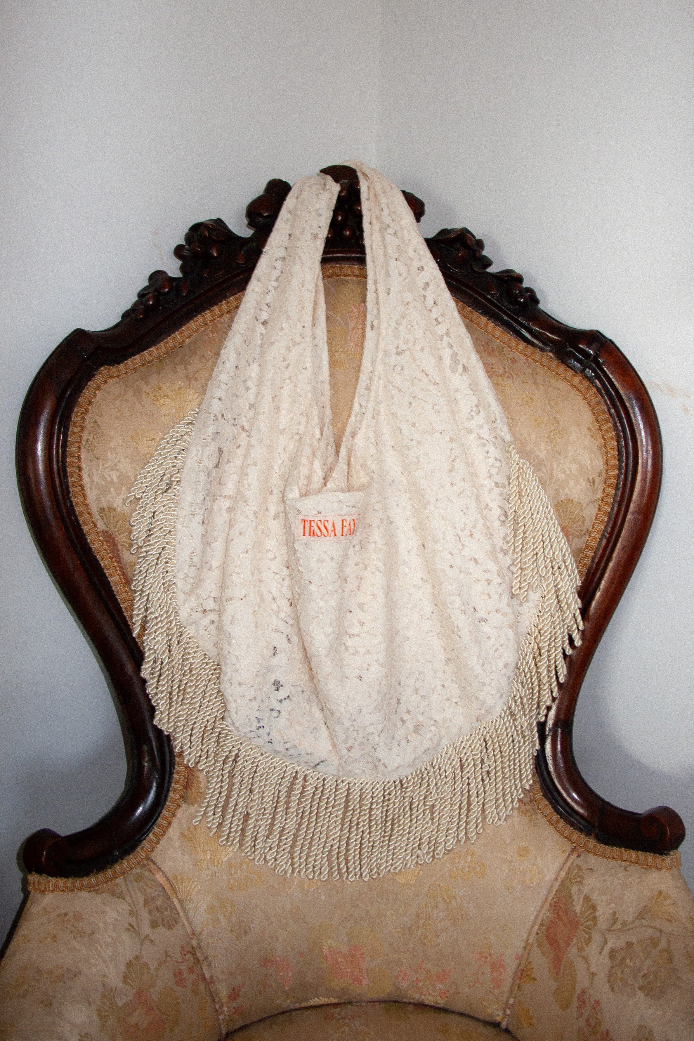 Cream lace tote bag with fringe on an ornate chair against a plain wall