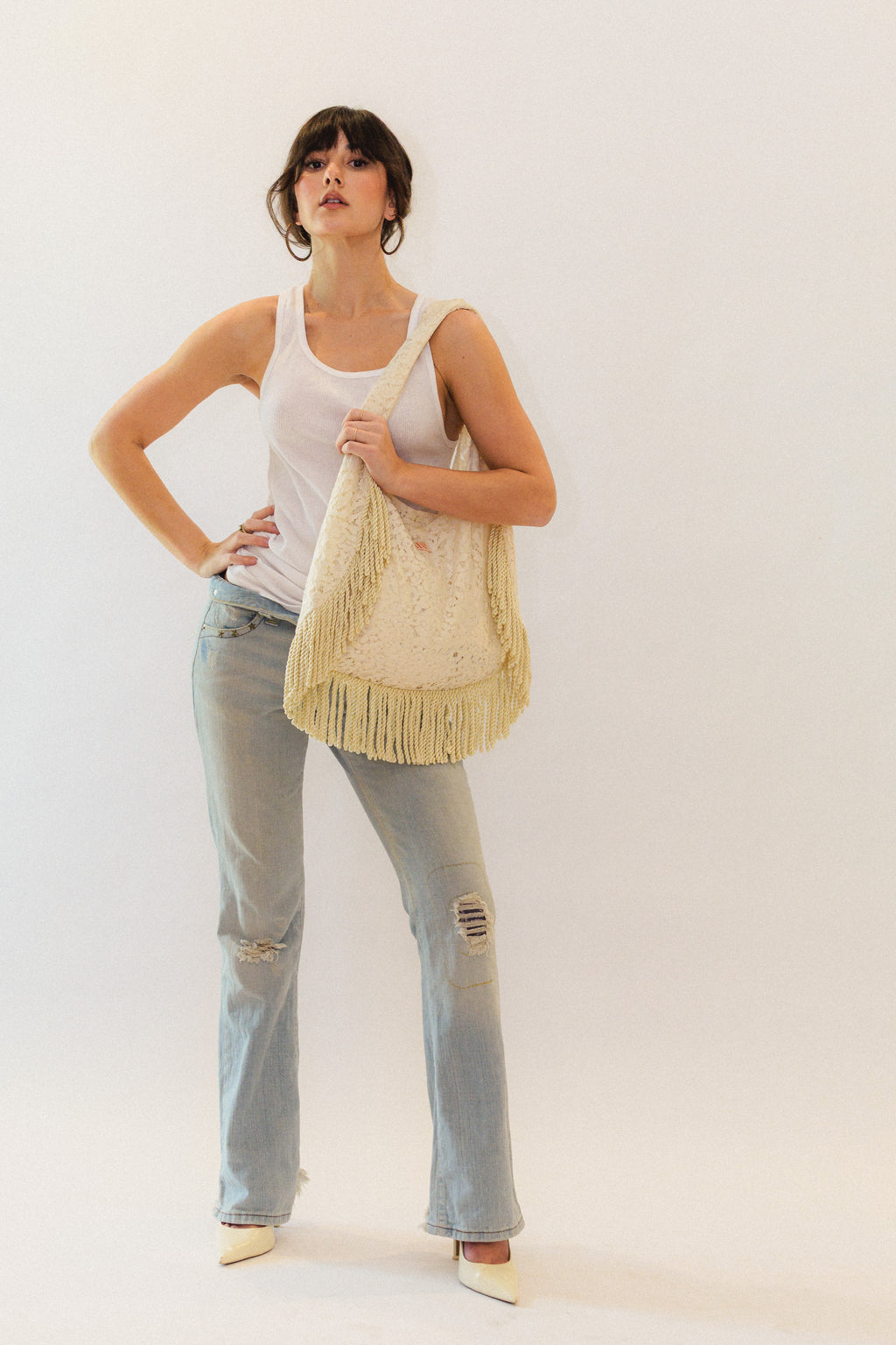 Woman holding a cream lace fringed tote bag against a white background