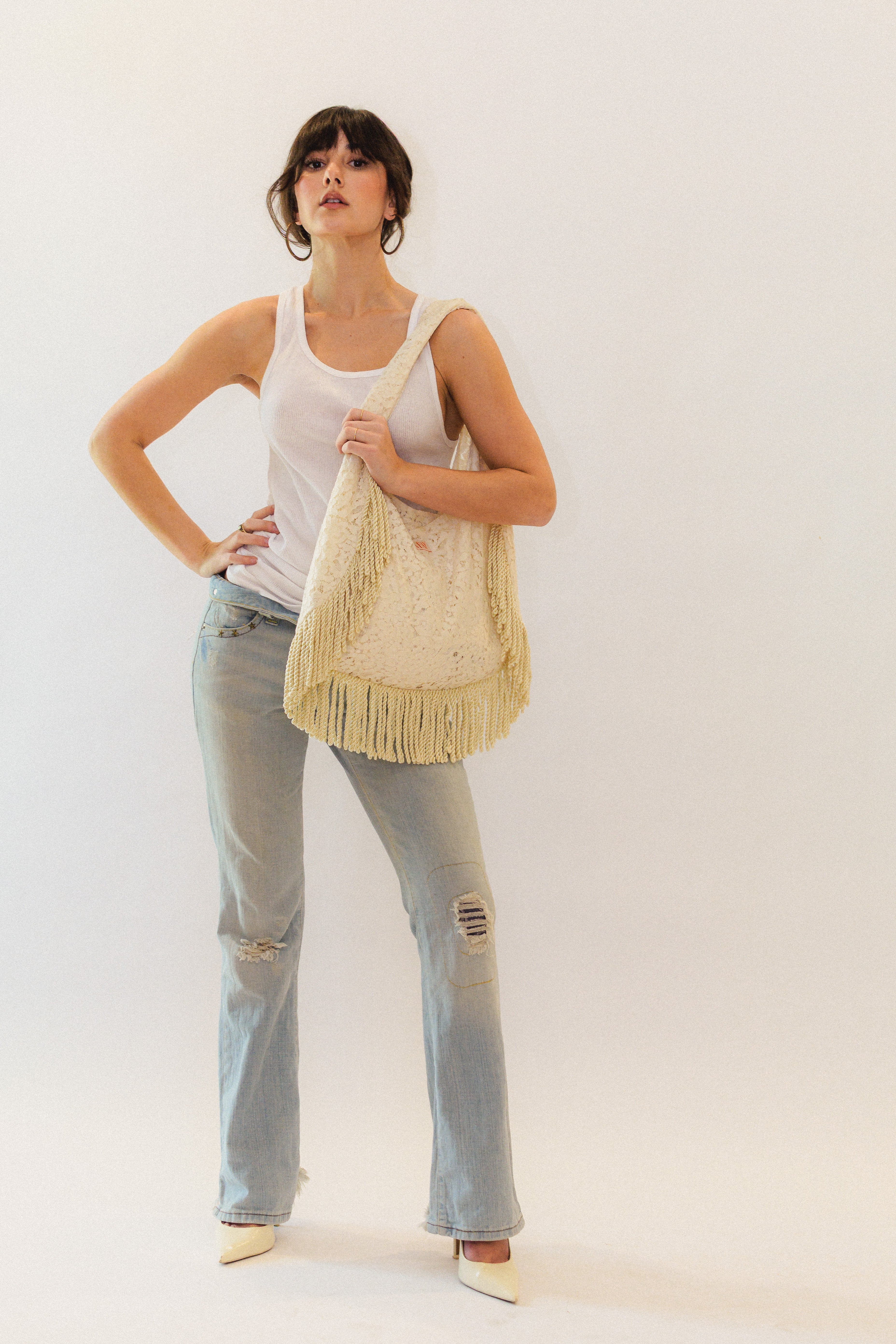 Woman holding a cream lace fringed tote bag against a white background
