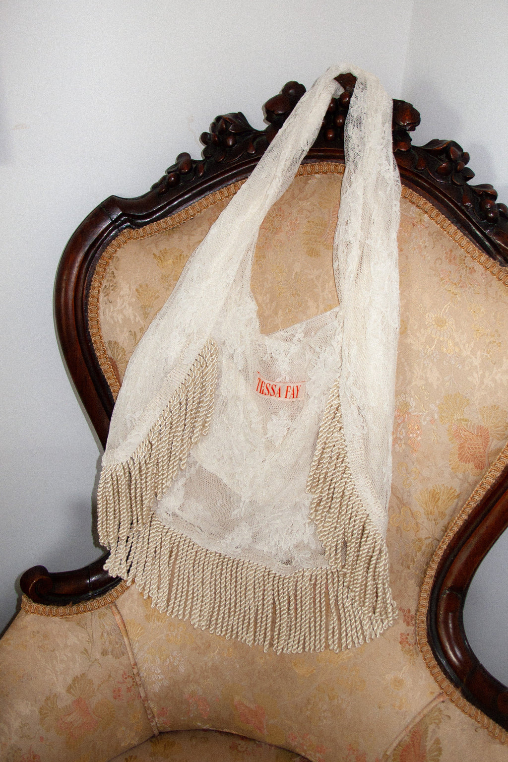 Cream lace mesh bag with fringe details on a vintage chair