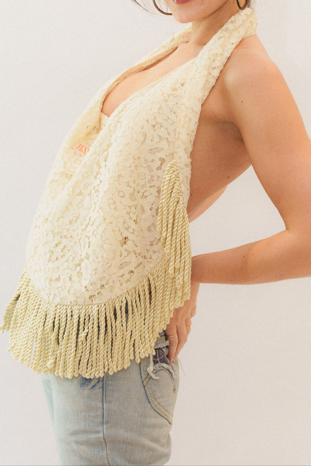 Woman wearing a cream fringe tote as a halter top on a plain background