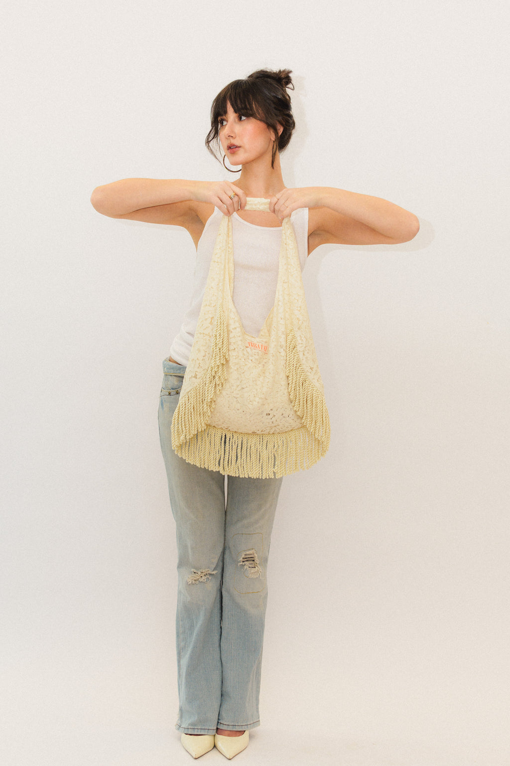 Woman holding a cream lace fringe tote bag against a plain background
