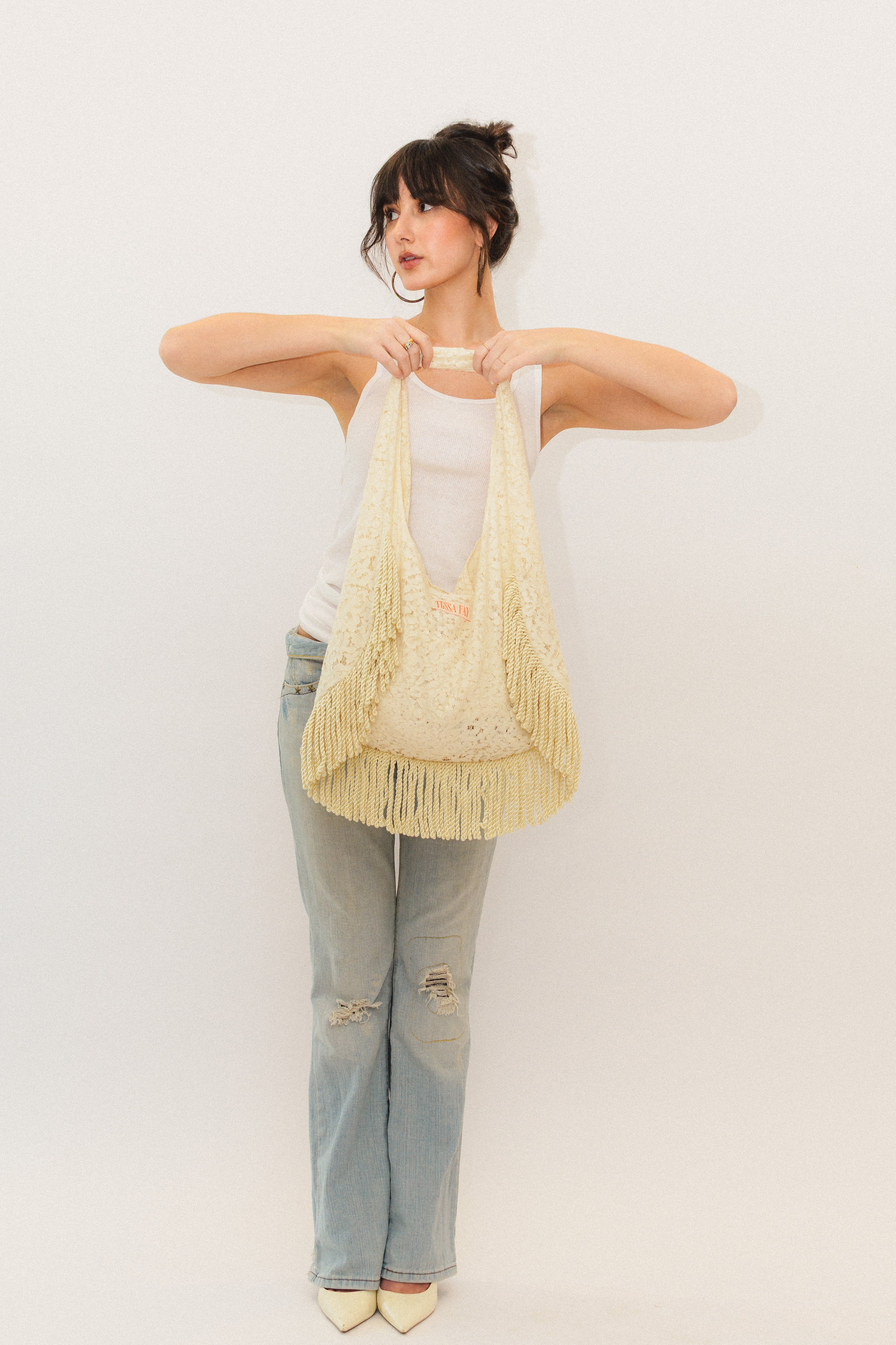 Woman holding a cream lace fringe tote bag against a plain background