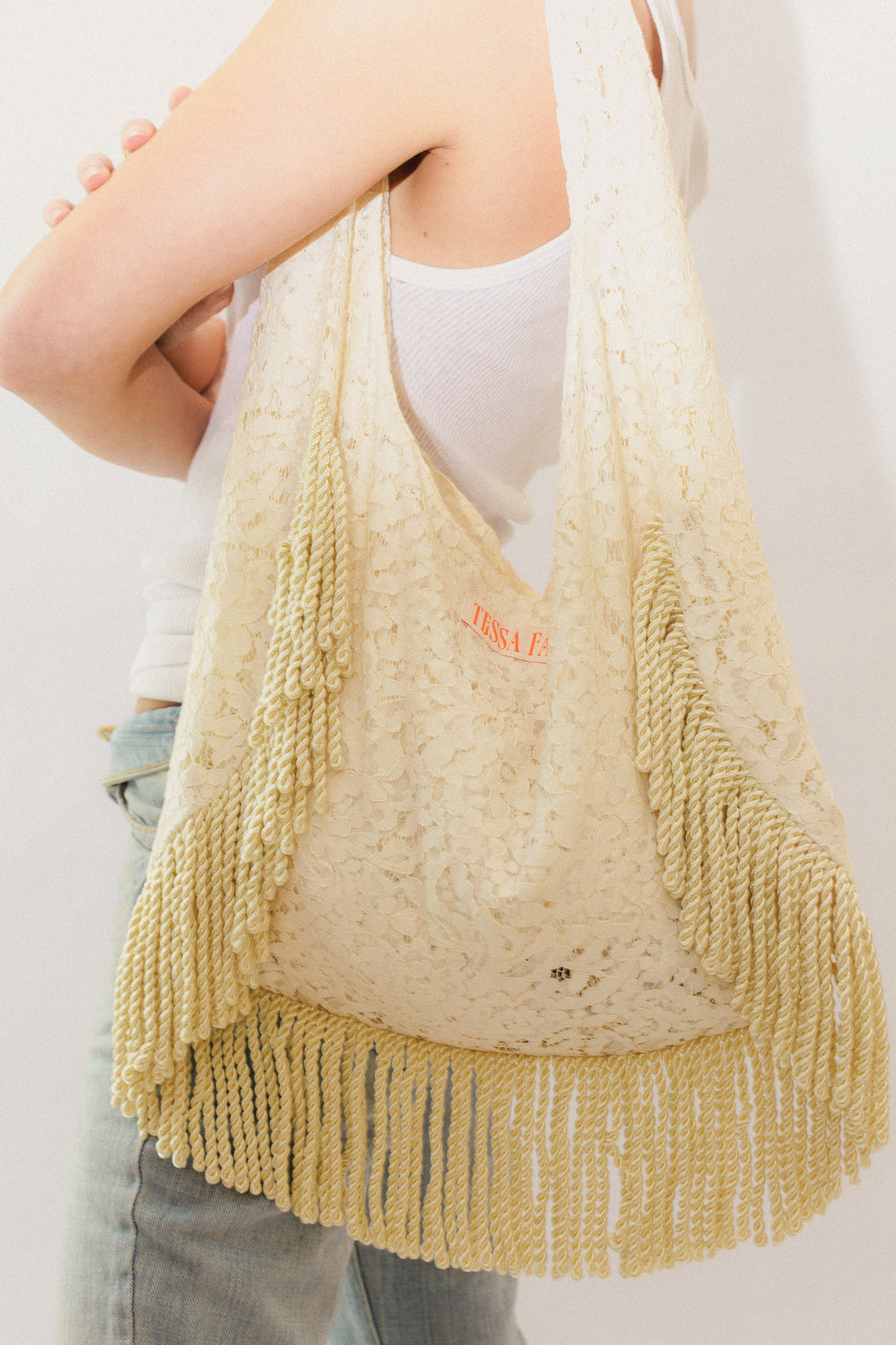 Cream lace bag with fringe held by a person against a plain background