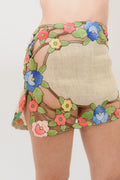 Close-up of a person wearing beige shorts with colorful floral embroidery and mesh side panels, shown against a light gray studio background.
